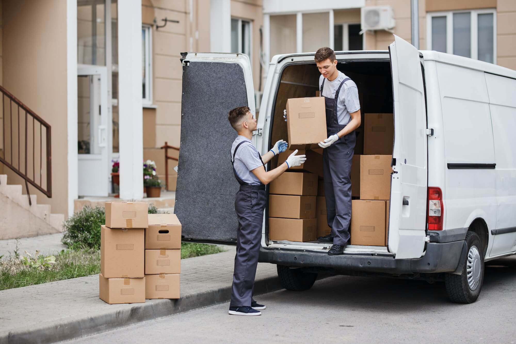 two young handsome movers wearing uniforms are unloading the van full of boxes house move mover 1